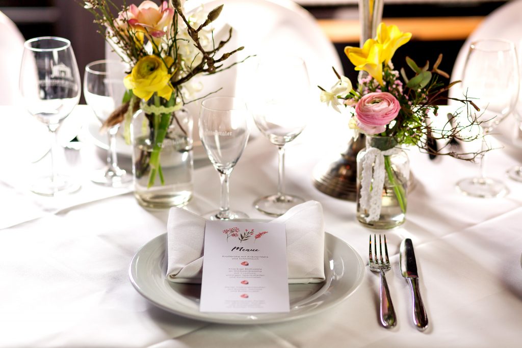 festliche Hochzeitstafel mit Menükarte und bunten Frühlingsblumen in Glasvasen